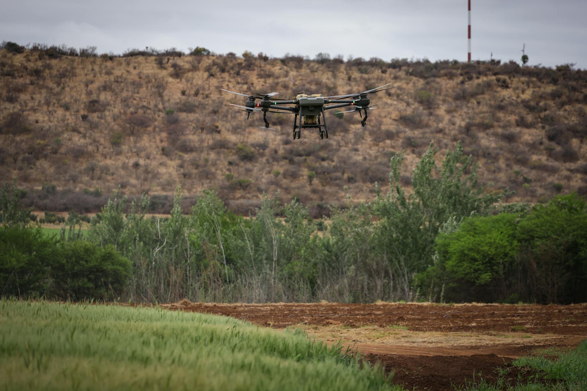 A drone flying over a lush agricultural field with hills in the background, showcasing modern farming technology.